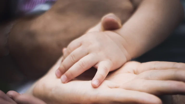 A baby's hand resting on the open palms of two parents